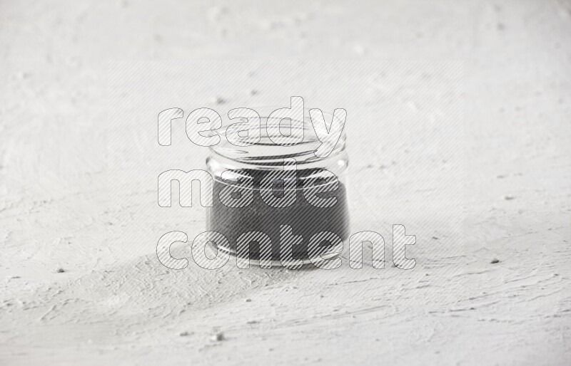 A glass jar full of black seeds on a textured white flooring
