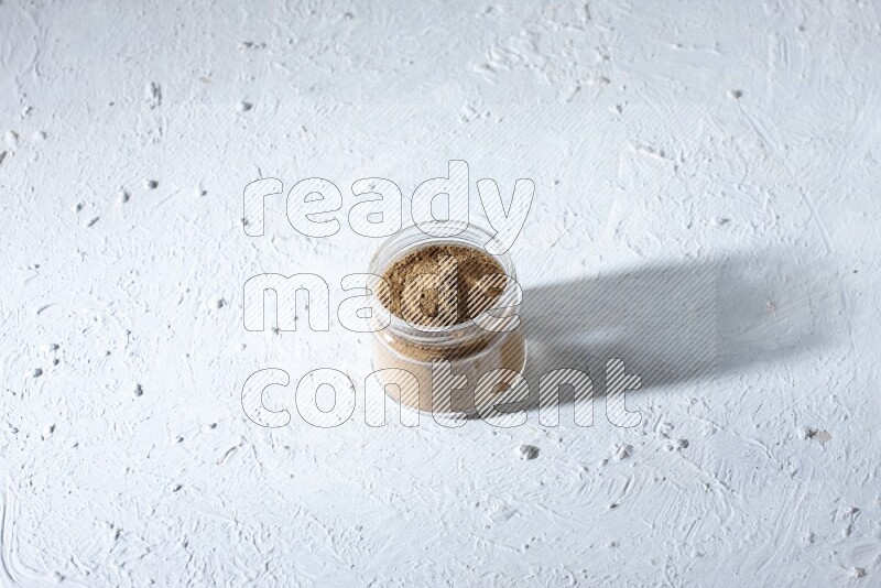 A glass jar full of allspice powder on a textured white flooring