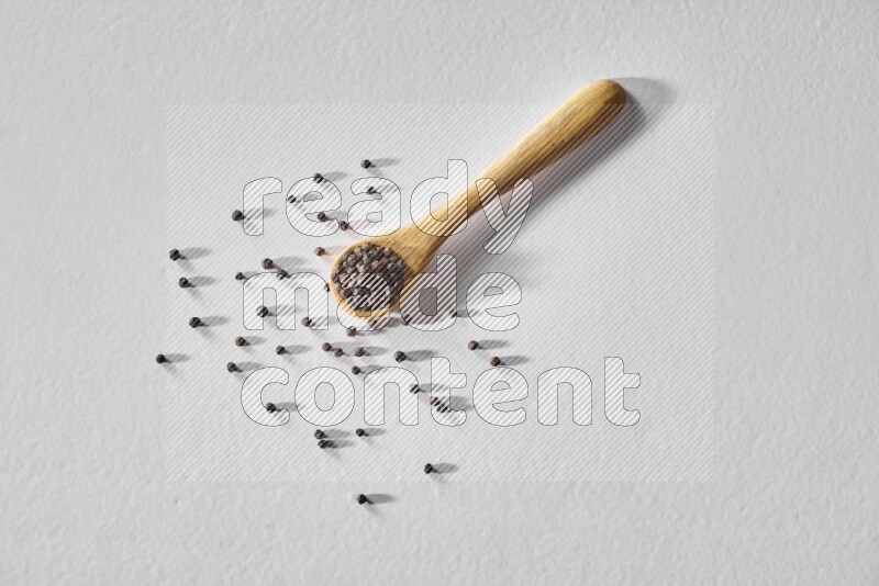 A wooden spoon full of black pepper on white flooring