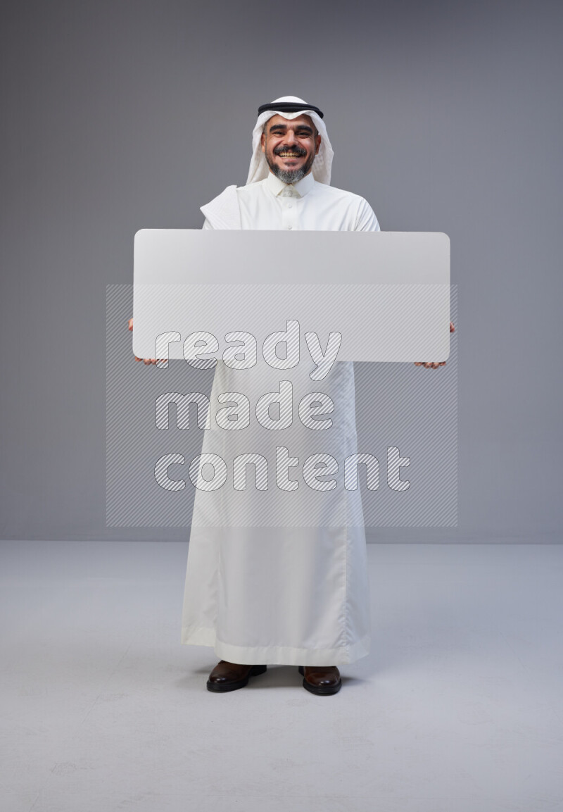 Saudi man Wearing Thob and white Shomag standing holding board on Gray background