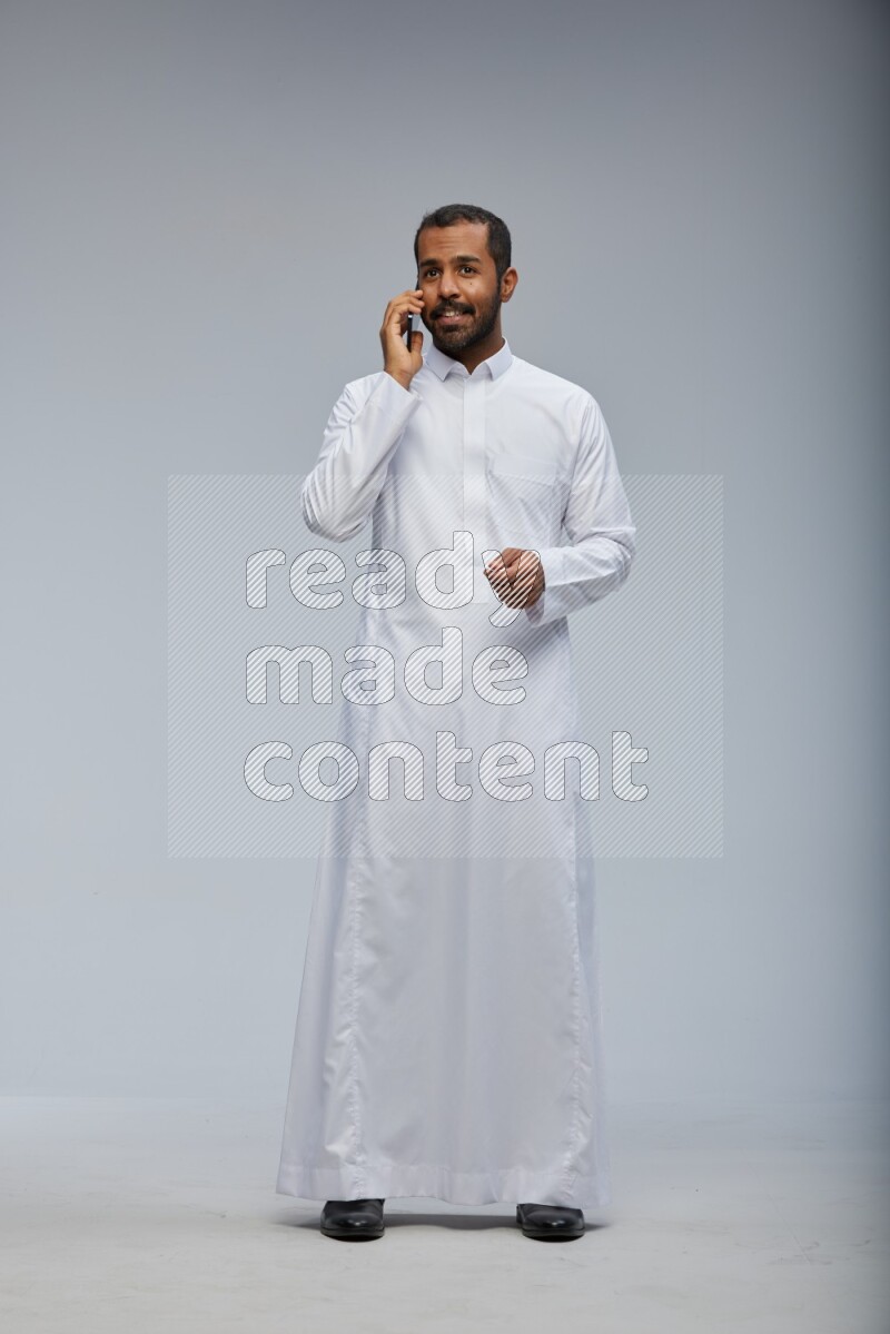 Saudi man wearing Thob standing talking on phone on Gray background