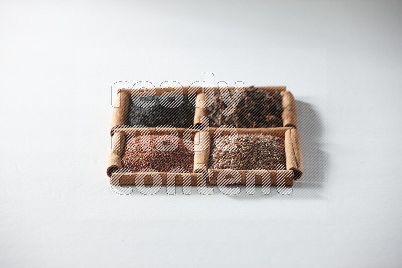 4 squares of cinnamon sticks full of black seeds, cloves, flaxseeds and garden cress on white flooring