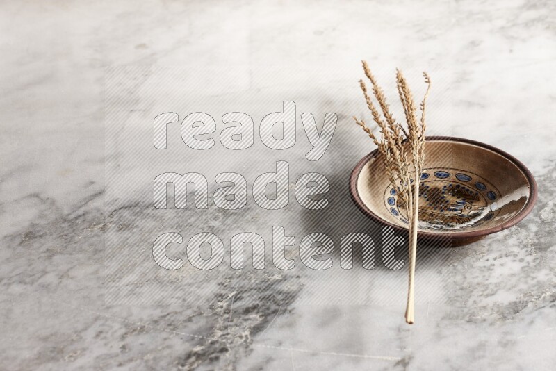 Wheat stalks on decorative pottery plate on grey marble background