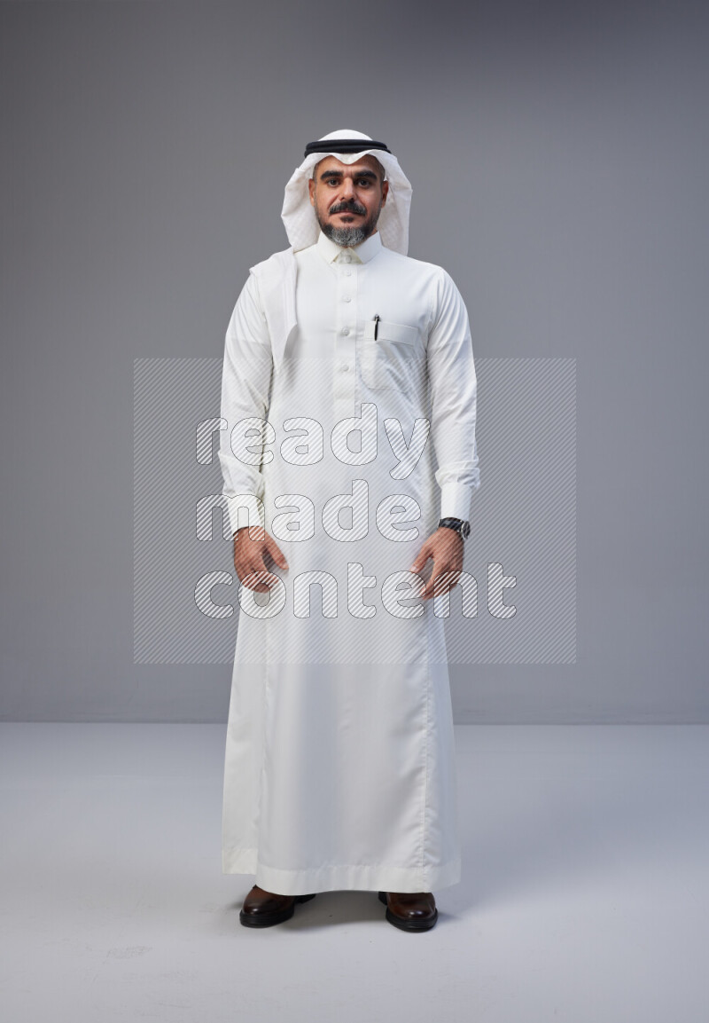 Saudi man Wearing Thob and white Shomag standing interacting with the camera on Gray background