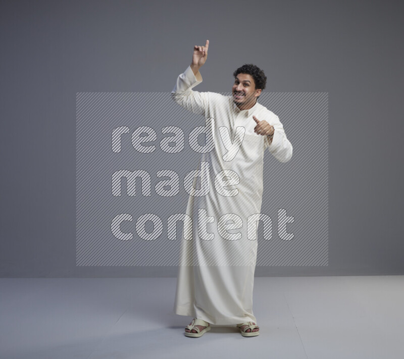 A Saudi man standing wearing thob interacting with the camera on gray background