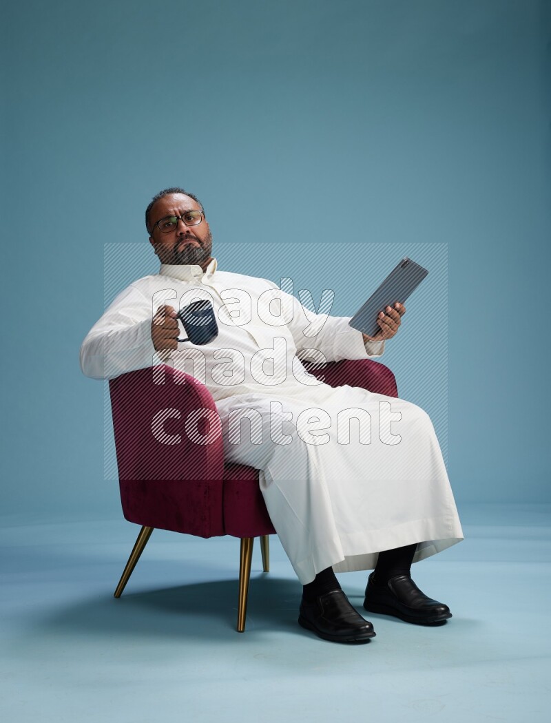 Saudi Man without shimag sitting on chair working on tablet on blue background