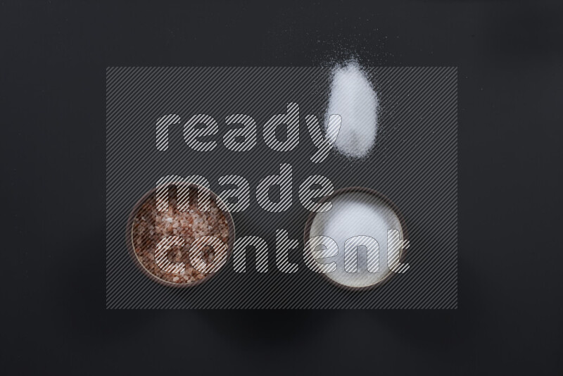 2 pottery bowls one is filled with himalayan salt and the other with white salt on black background
