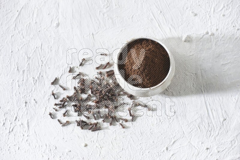 A beige ceramic bowl full of cloves powder and whole cloves on a white flooring