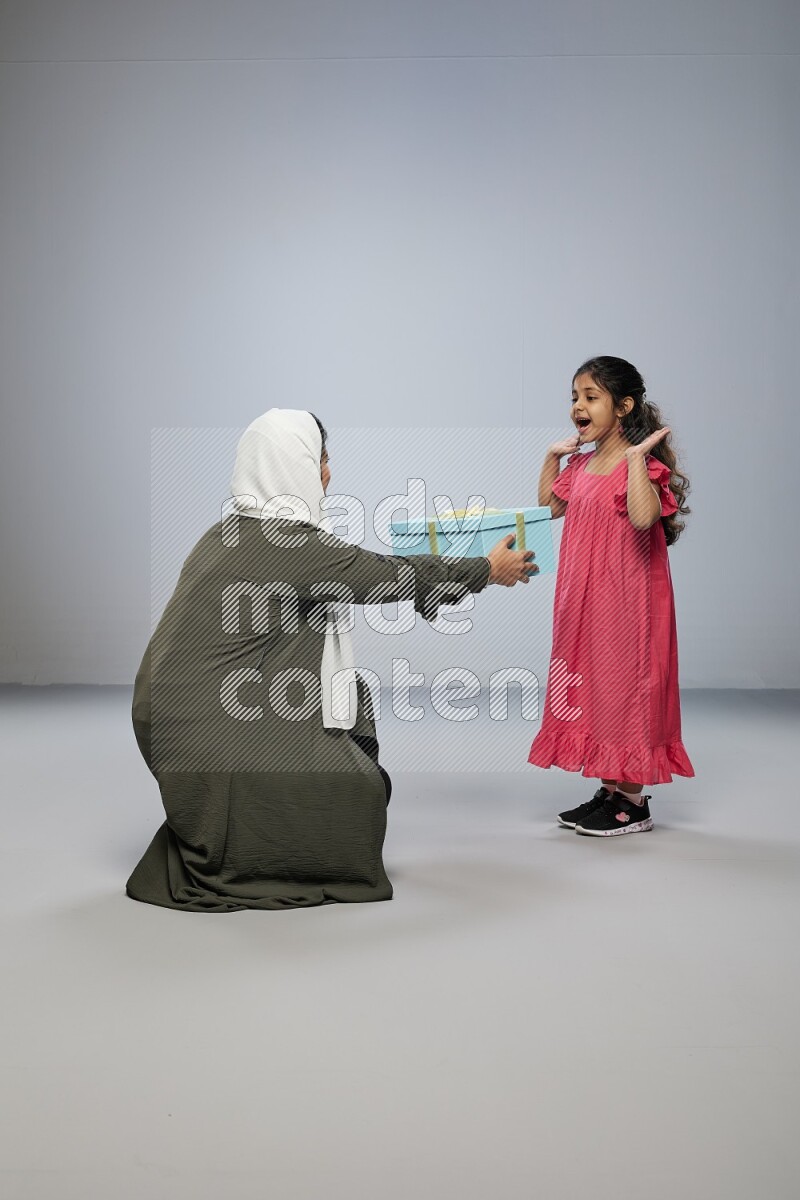 A girl giving a gift to her mother on gray background