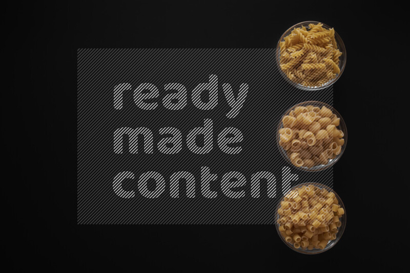 Different pasta types in 3 glass bowls on black background