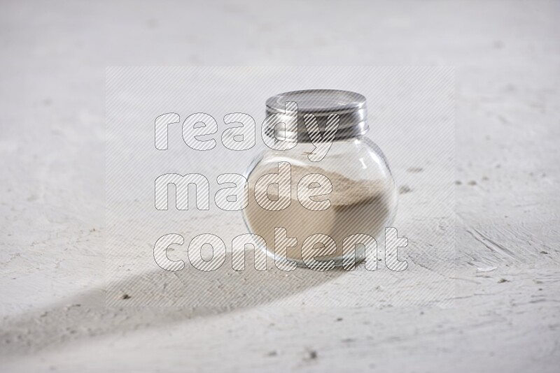 A glass spice jar full of garlic powder on a textured white flooring