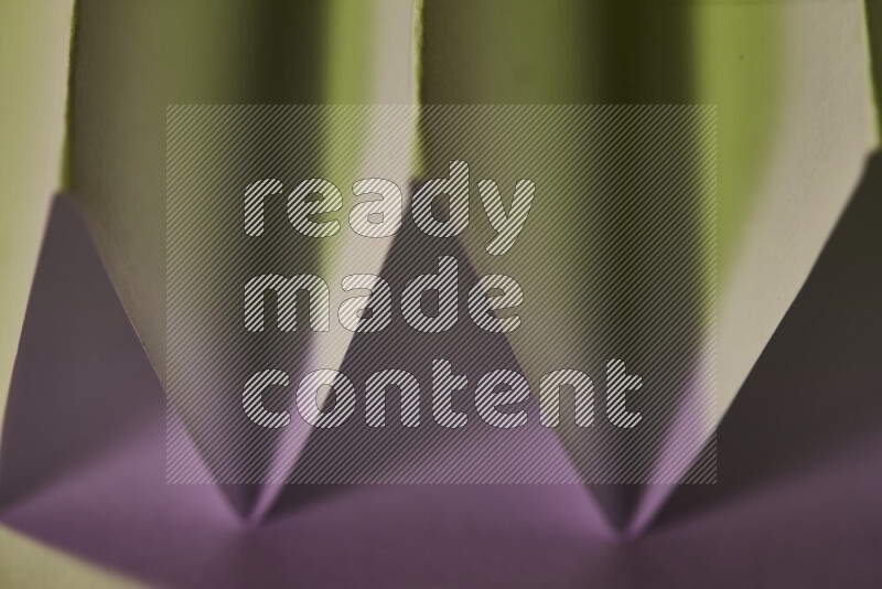 A close-up abstract image showing sharp geometric paper folds in green and pink gradients