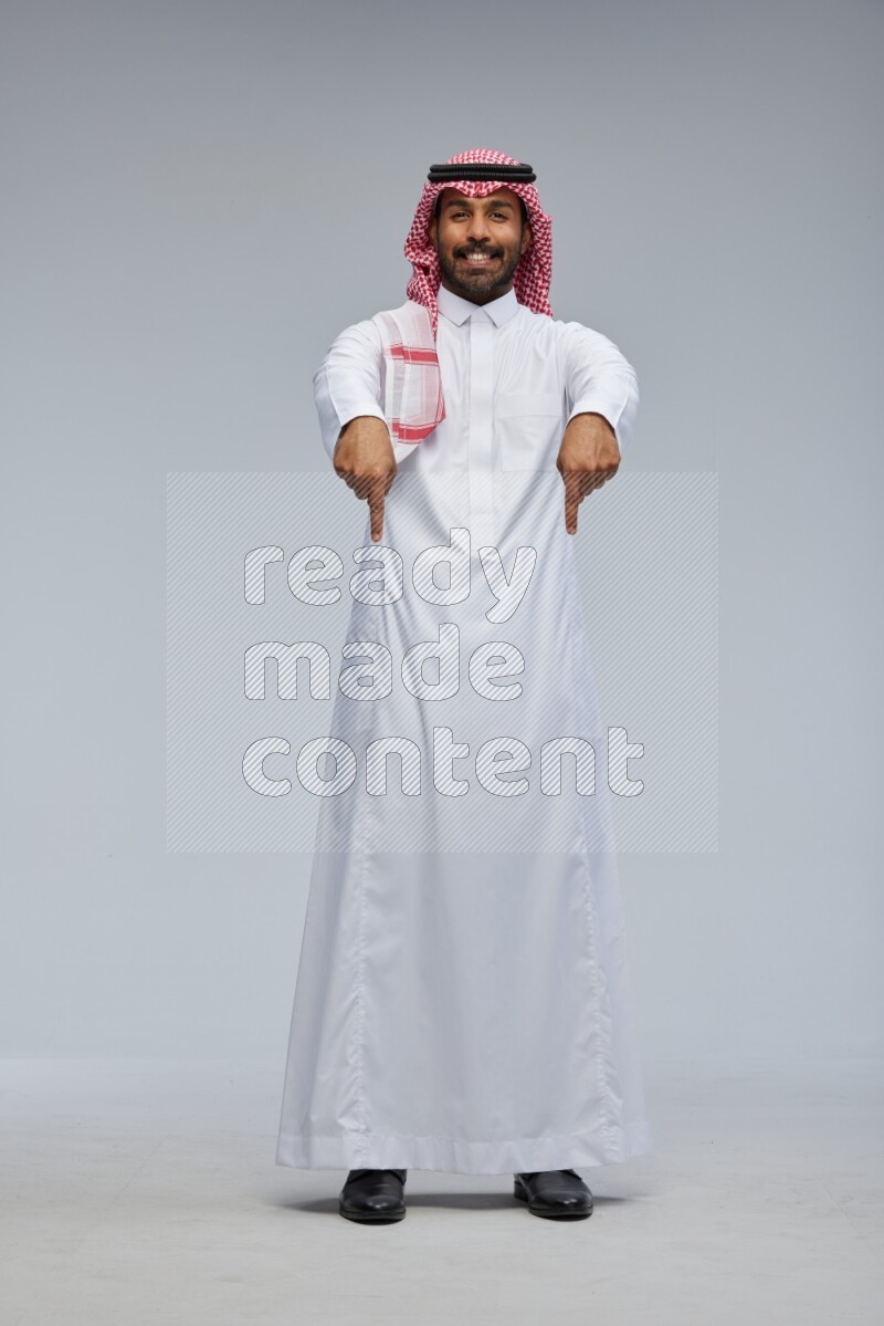 Saudi man Wearing Thob and shomag standing interacting with the camera on Gray background