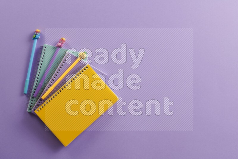 Multicolored notebooks with different school supplies on purple background