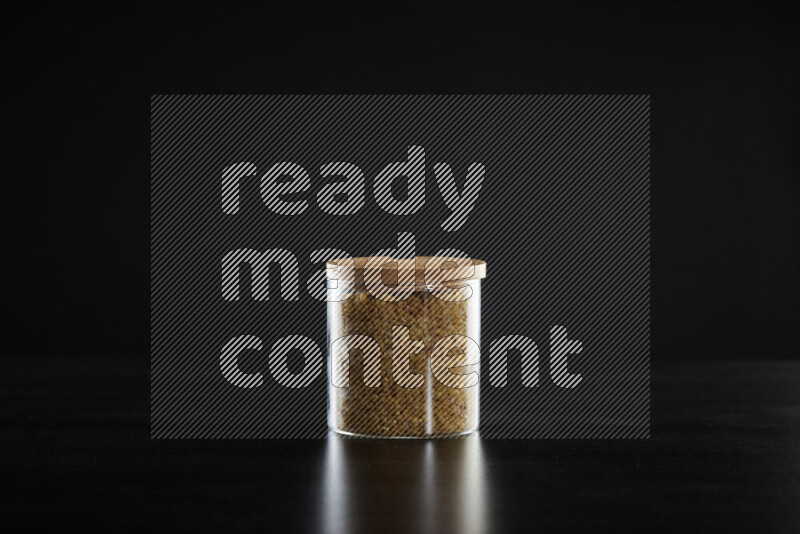 Coarse bulgur in a glass jar on black background