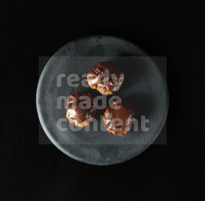 Assorted desserts in a black pottery plate on black background