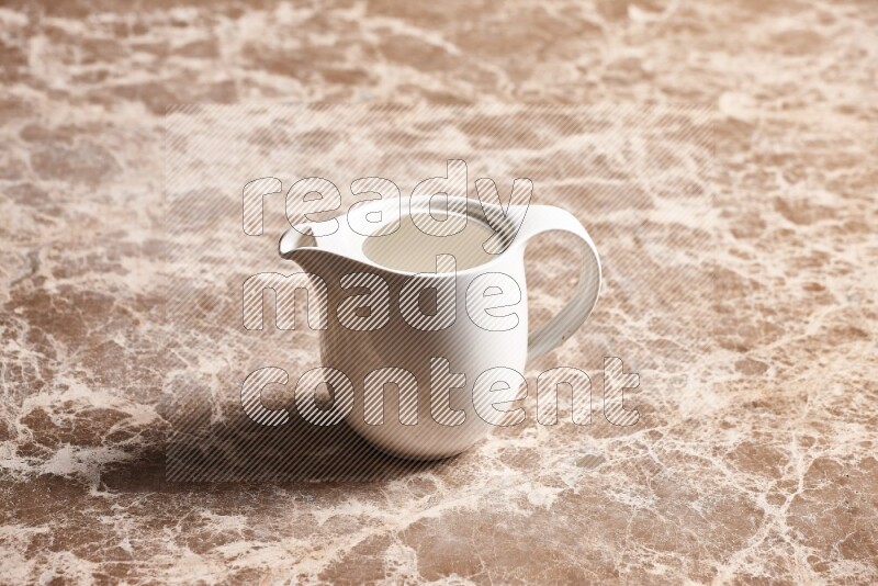 A ceramic milk jug on beige marble background