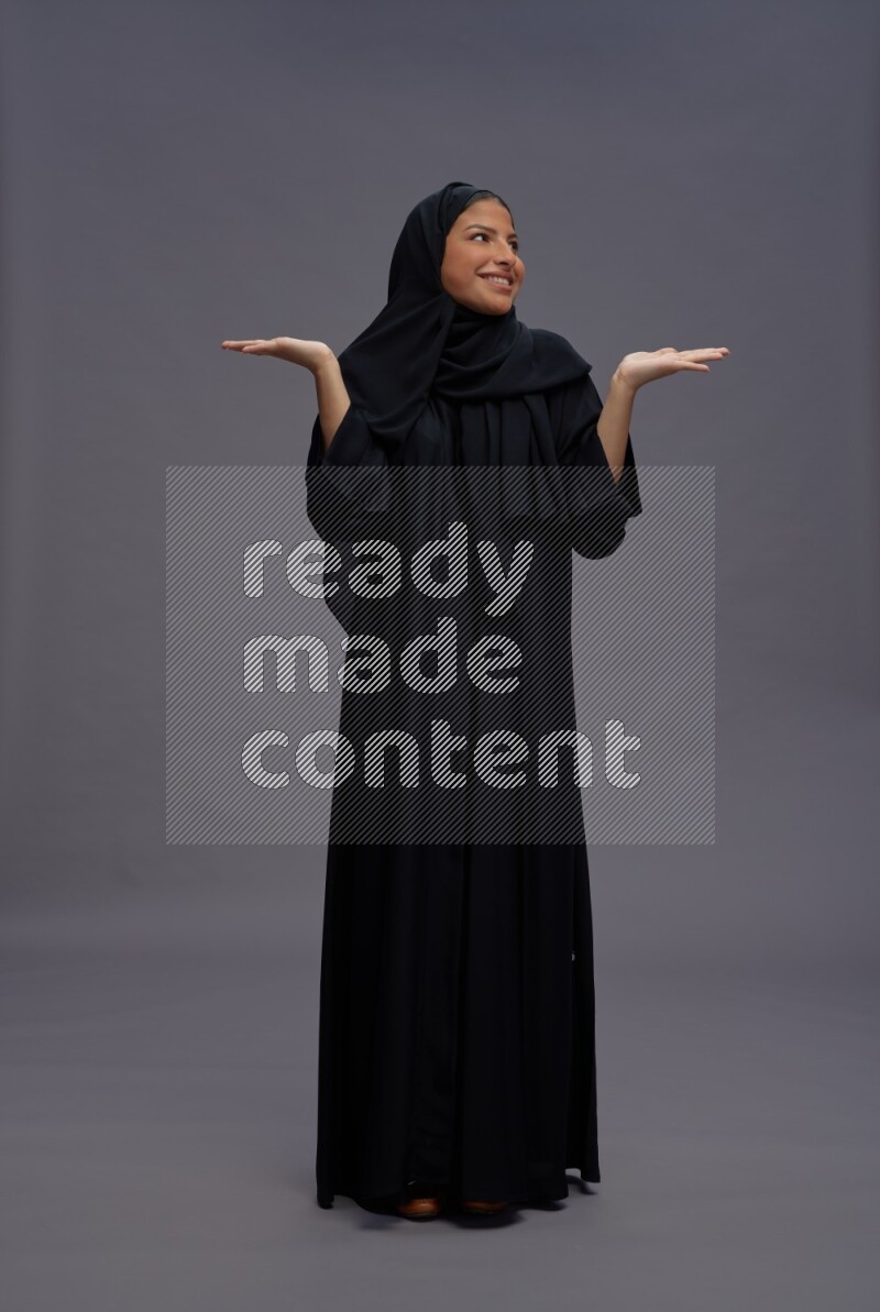 Saudi woman wearing Abaya standing interacting with the camera on gray background