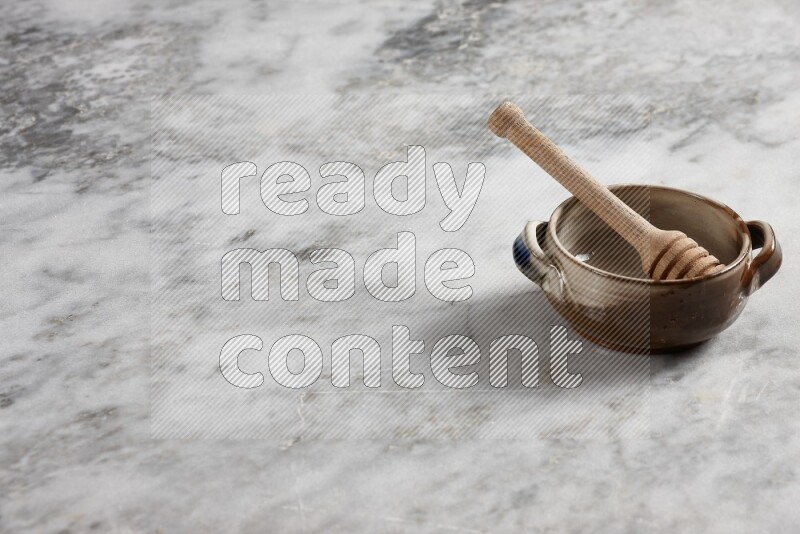 Multicolored pottery bowl with wooden honey dipper in it on grey marble background