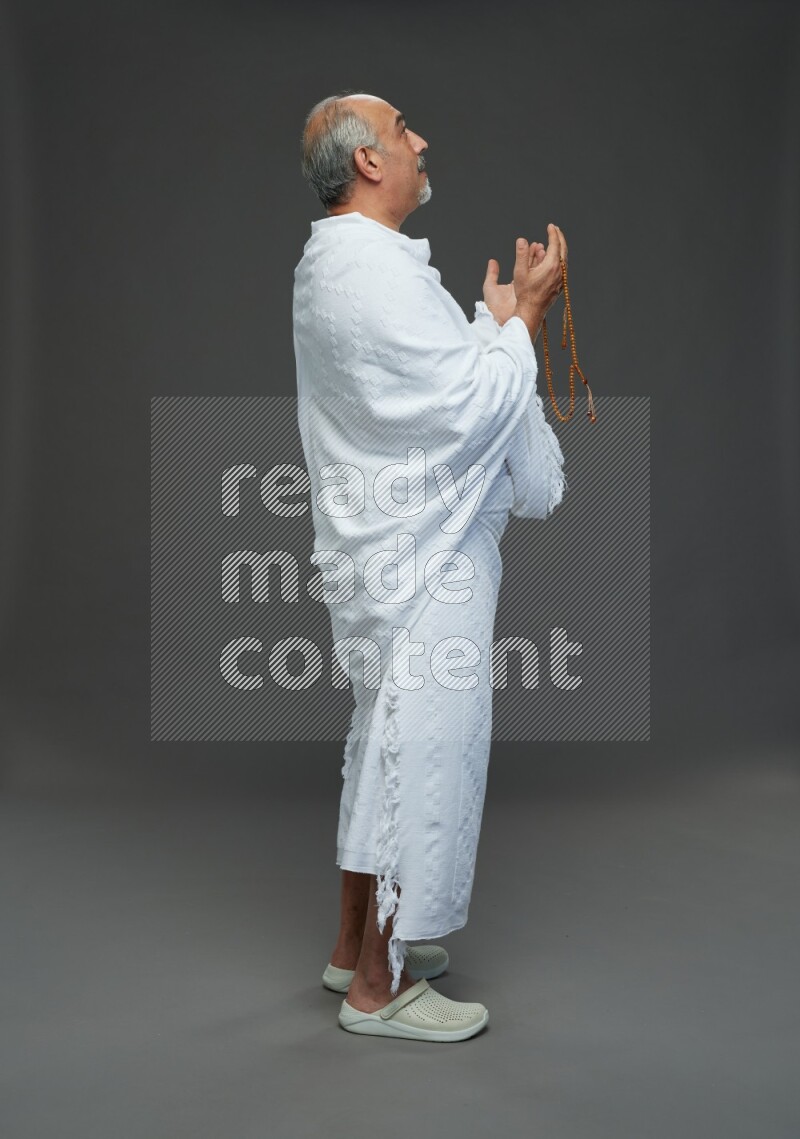 A man wearing Ehram Standing dua'a on gray background