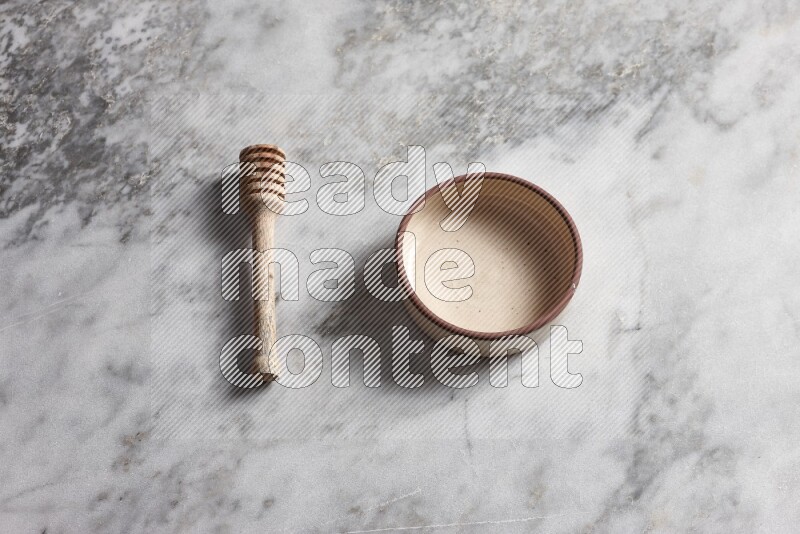 Beige pottery oven bowl with wooden honey dipper on the side on grey marble background