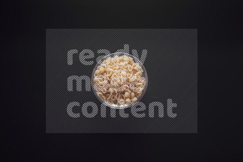 Shells pasta in a glass bowl on black background