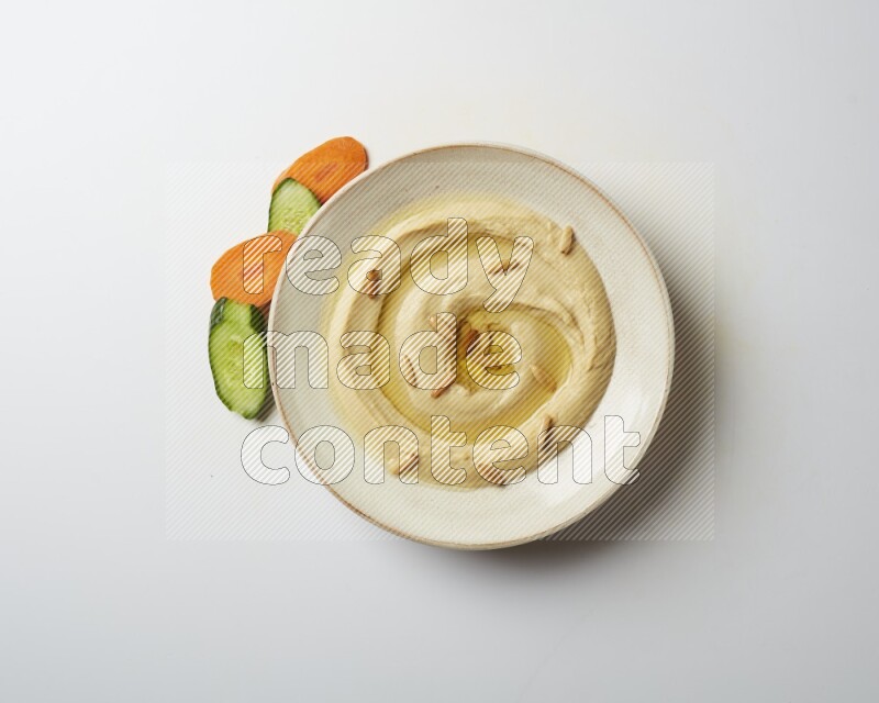 Hummus in a pottry plate garnished with pine nuts on a white background
