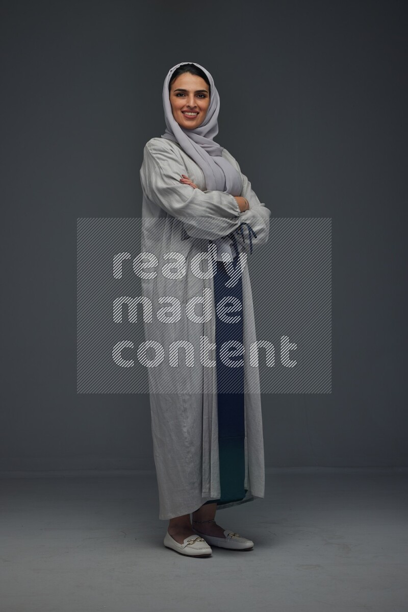 A Saudi woman wearing a light gray Abaya and head scarf standing and making multi poses eye level on a grey background