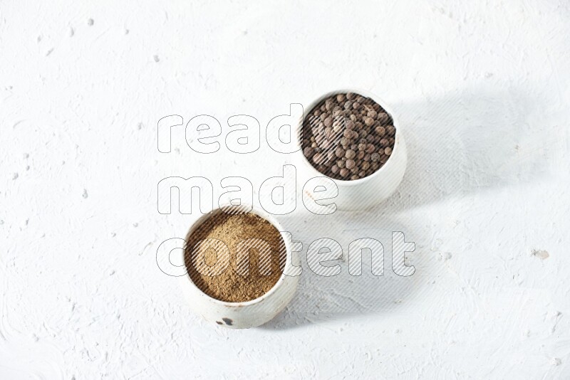 وعاءان بيج، أحدهما ممتلئ ببودرة بهار الفلفل الحلو والآخر بحبوبه، على خلفية بيضاء