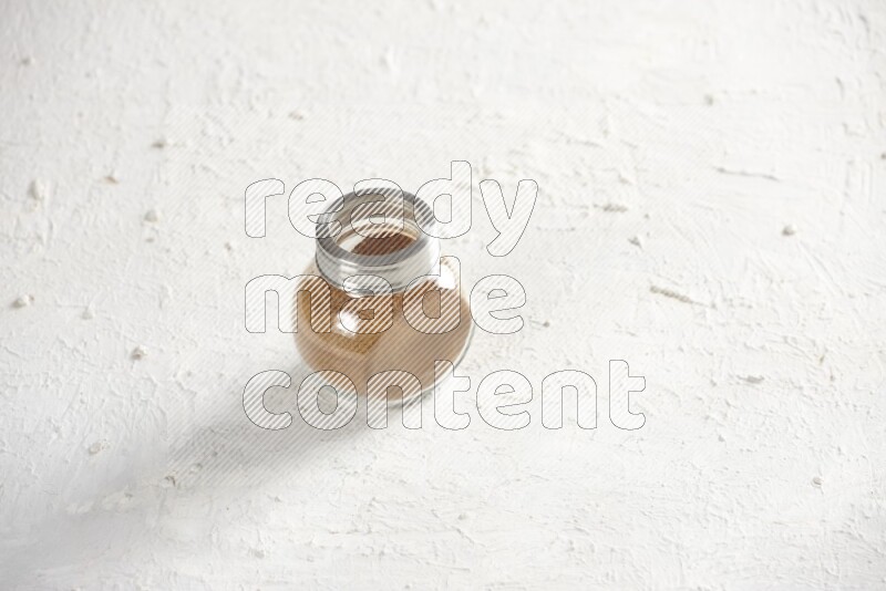 Herbs glass jar full of cinnamon powder on a textured white background