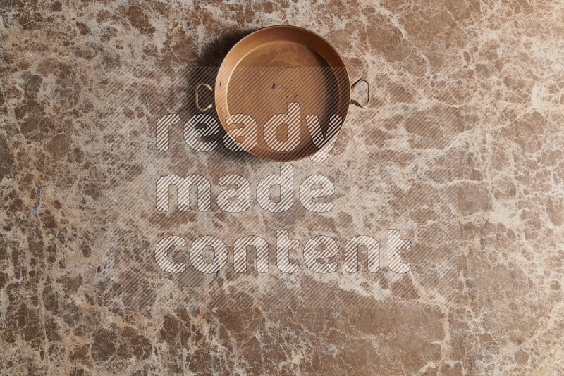 A small copper pan on beige marble background