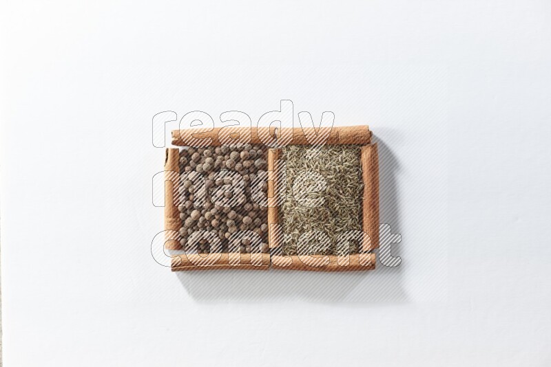 مربعان من أعواد القرفة ممتلئان ببهار الفلفل الحلو والكمون علي خلفية بيضاء