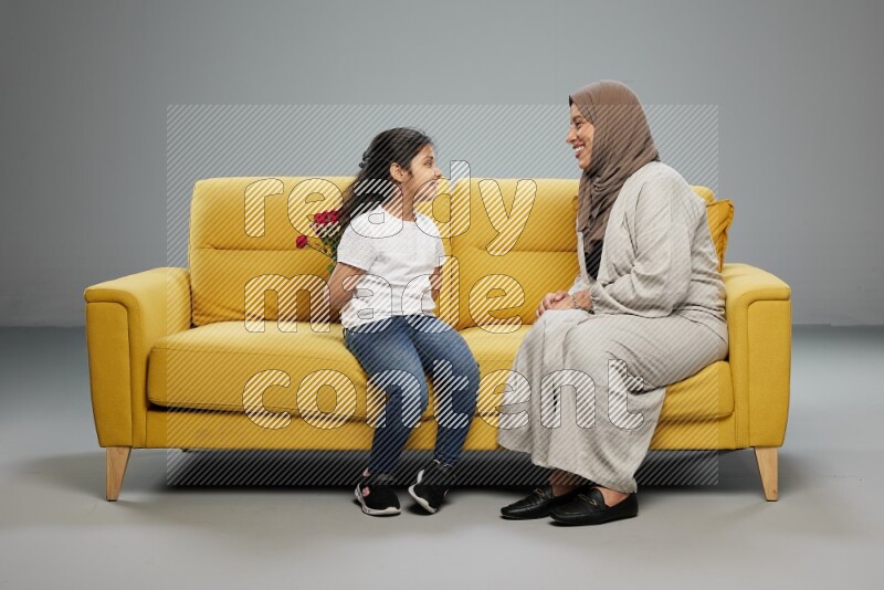 A girl sitting hiding flowers behind her back for her mother on gray background