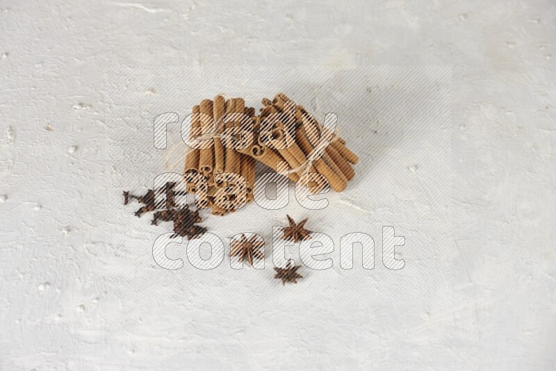 Two bounded stacks of cinnamon sticks with cloves and star anise on white background
