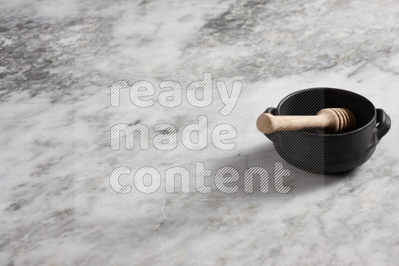 Black pottery bowl with wooden honey dipper in it on grey marble background