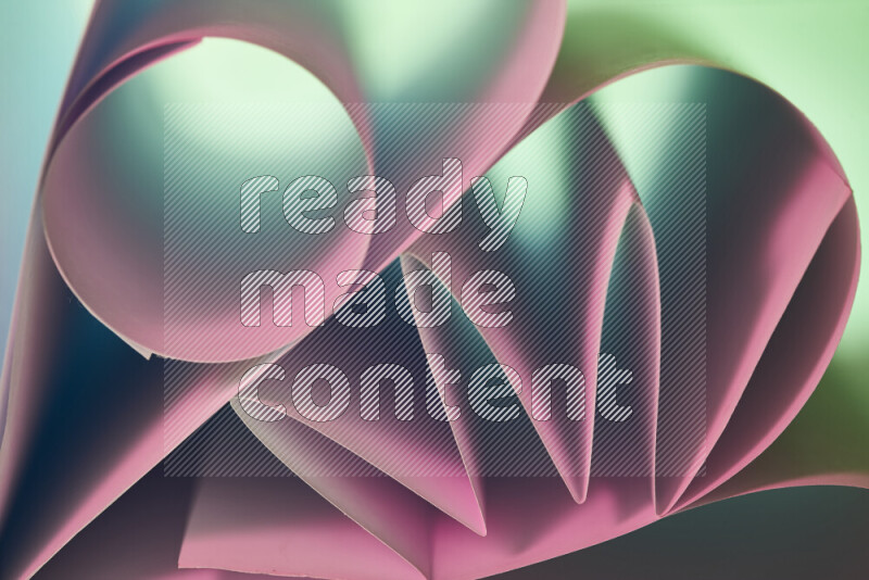 An artistic display of paper folds creating a harmonious blend of geometric shapes, highlighted by soft lighting in green and pink tones
