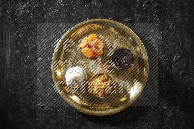 Dried fruits in metal bowls with tamarind on a tray in dark setup