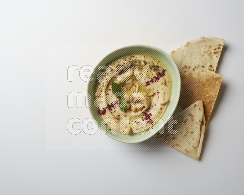 Hummus in a green plate garnished with zattar & sumak on a white background