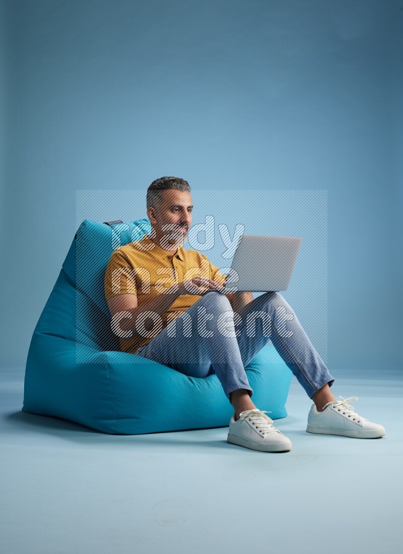 A man sitting on a blue beanbag and working on laptop