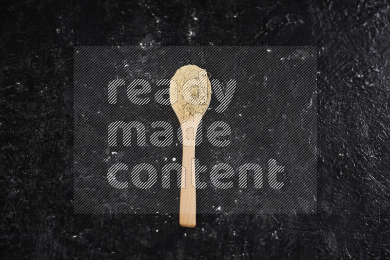 A wooden spoon full of ground ginger powder on black background