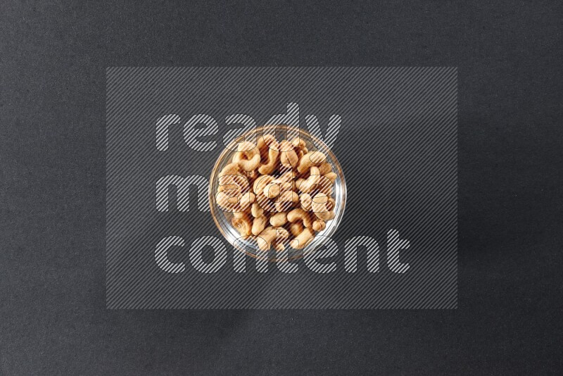 A glass bowl full of cashews on a black background in different angles