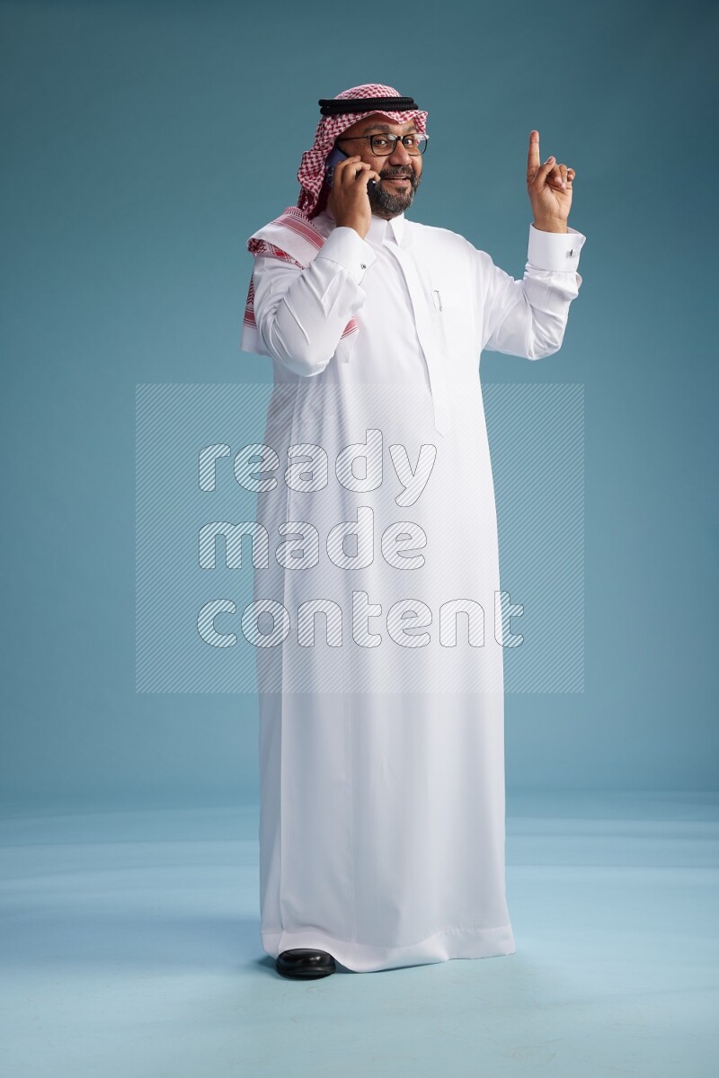 Saudi Man with shimag Standing talking on phone on blue background