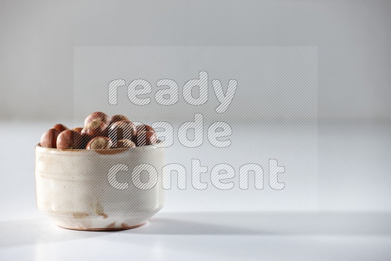 A beige ceramic bowl full of hazelnuts on a white background in different angles