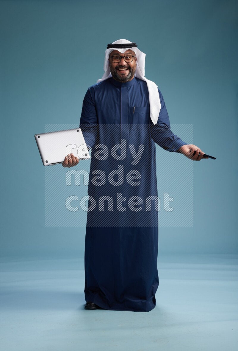Saudi Man with shimag Standing texting on phone on blue background