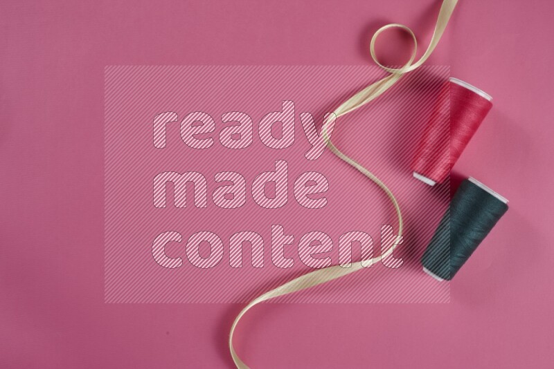 A green and pink collection of sewing and tailoring tools arranged on a pink background