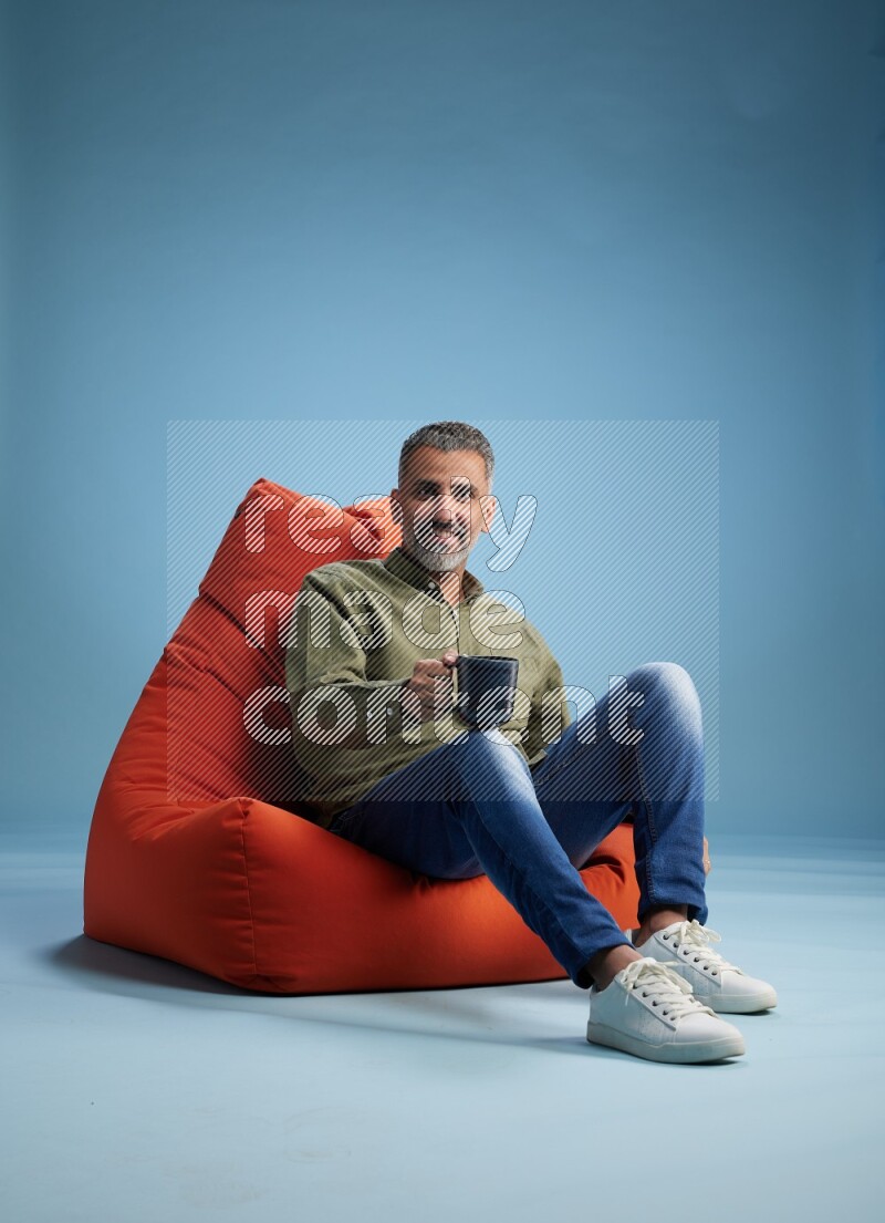 A man sitting on an orange beanbag and drinking coffee