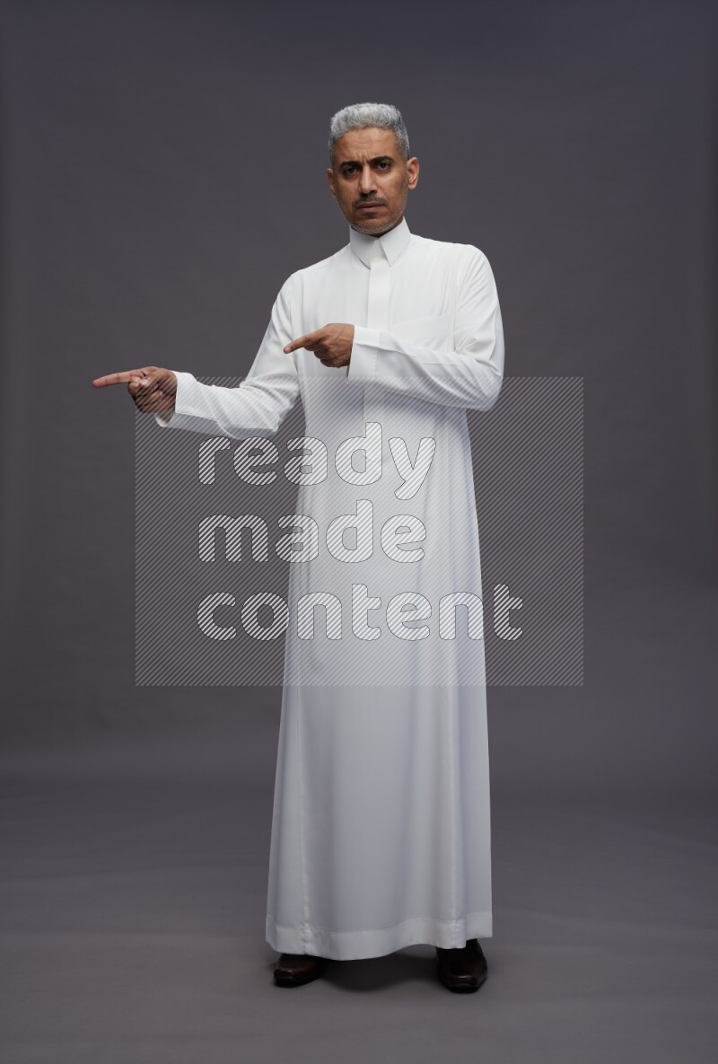 Saudi man wearing thob standing interacting with the camera on gray background