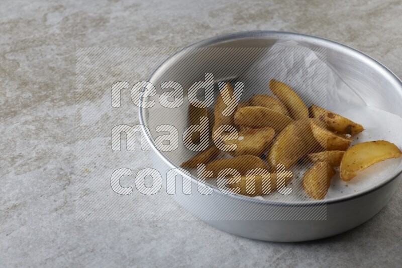 wedges potato on parchment paper in a stainless steel round tray on grey textured counter top