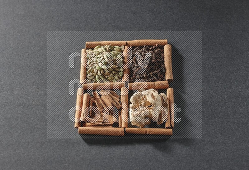 4 squares of cinnamon sticks full of cinnamon, cardamom, cloves and dried ginger on black flooring
