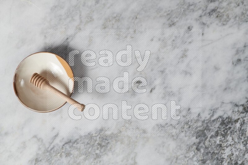 طبق فخاري متعدد الألوان مع ملعقة عسل خشبية بداخله على خلفية من الرخام الرمادي